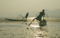 Silhouettes of two Intha fishermen with Sun s reflection on water.Myanmar