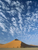 Sand dune with dramatic clouds scattered in a blue sky above seen in early morning light