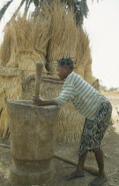 Near Garango. Young girl pounding grain with straw roofs and granaries behindGirl called Mariam
