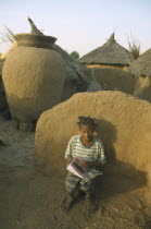 Near Garango.Young girl called Mariam sat against wall doing her homework with grain store and village houses behind.