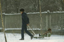 Father pulling child on sledge through the snow  both wrapped up against the cold.