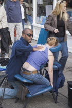 Masseur performing massage in East Street on a woman customer sat head down in a massage chair.