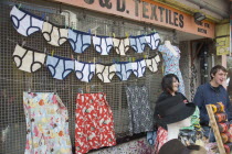 A North Lanes market stall selling hats and clothes with a  large colourful display of underwear behind two young smiling stall holders.
