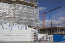 Housing construction site with advertising billboard on view next to road and a large crane in the background.