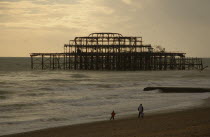The ruined West Pier with a man and small child walking together along shoreline.