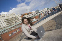 Woman using a laptop to surf the internet  in the free WiFi zone on the beach between the piers