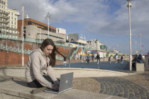 Woman using a laptop to surf the internet  in the free WiFi zone on the beach between the piers