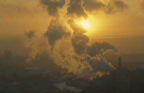 Setting sun partly obscured by plume of thick smoke from industrial chimney.air pollution