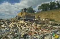 Bulldozer on heap of rubbish in landfill site.