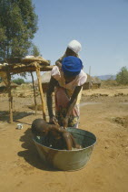 Woman carrying child on her back washing another in tin bath on farm.