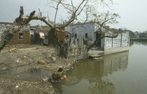 Woman washing pot in polluted water of slum with dung used for fuel drying on walls of delapidated buildings behind. Kolkata