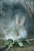 Azande tribeswoman kneeling over fire to purify herself after giving birth.
