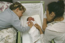 Mother and five year old son looking at week old sister lying in cot.