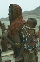 Danakil tribeswoman carrying baby on her back in sling decorated with cowrie shells used for barter.