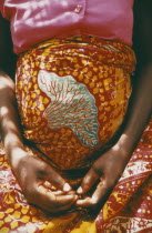 Cropped shot of woman thirty six weeks pregnant wearing brightly coloured sarong and with her hands folded in her lap beneath her belly.Colored Leis
