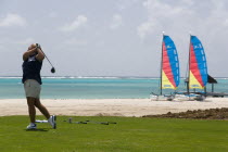 Lady golfer teeing off on the Raffles hotel practice range with beach and hobbie cats behindwoman golf