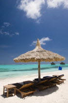 Palapa thatched shelter and sunbeds on Godahl Beach at Raffles Resort with offshore treatment rooms of the Amrita Spa beyond