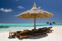 Palapa thatched shelter and sunbeds on Godahl Beach at Raffles Resort with offshore treatment rooms of the Amrita Spa beyond