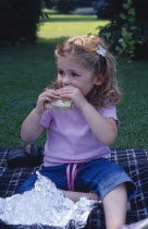 The Bishops Palace Gardens.  Girl aged three eating brown bread and lettuce sandwich during picnic lunch.