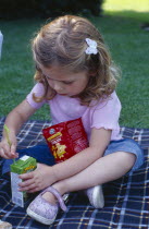 The Bishops Palace Gardens.  Girl aged three putting straw into carton of low sugar blackcurrant juice drink during picnic lunch.