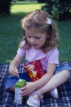 The Bishops Palace Gardens.  Girl aged three putting straw into carton of low sugar blackcurrant juice drink during picnic lunch.