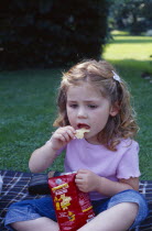 The Bishops Palace Gardens.  Girl aged three eating potato crisp snack during picnic lunch.