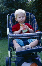 The Bishops Palace Gardens.  Boy aged one and a half drinking from carton of low sugar blackcurrant drink while sitting in pushchair during picnic lunch.