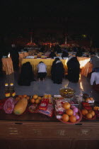 Morning prayers in the main prayer hall. Kneeling worshippers with table in foreground spread with offerings of fruit flowers and candles.Monastery of Supreme Bliss Center Centre Colored Coloured