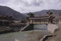 Chinese bridge with pagoda style roof over river in mountain landscape