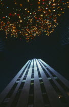 View looking upwards from the ground at brightly lit christmas tree and sky scraper toward the night sky