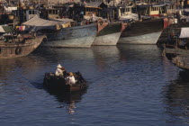 People in a small motor boat passing in front of fishing boats moored in the harbour
