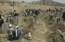 Moslems paying respects to the dead in graveyard surrounded by barren hillside.