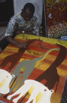 Local artist working on painting in the Tingatinga style depicting African animals in bold colours.
