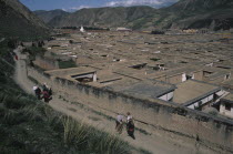 View over the rooftops of the Labrang Monastery with people walking a path running alongside the exterior wall