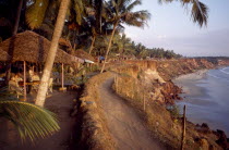 Coastal path along cliff tops with sandy beach below and woman sitting under thatched restaurant shade