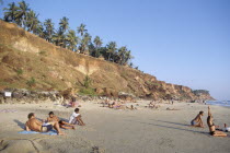 Sun bathers on sandy beach surrounded by small cliffs topped with palms
