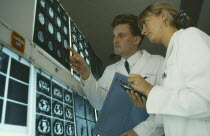 Male and female doctors examine brain scans on wall mounted light boxes