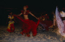 Women in red costume dancing on the beach at night. Sega is the national dance and music form of Mauritius.