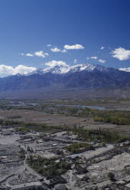 General view over the valley and River Indus with scattered buildings in the foreground and snow capped mountains on the horizon