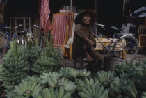 Smiling woman sitting behind display of green Bananas