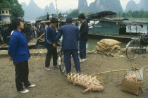 Villagers loading boats after market with pig in basket in the foreground.
