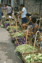 Village vegetable market  line of vendors selling beans and aubergines displayed in baskets in front of them.