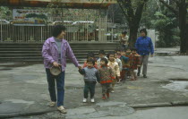 Line of nursery school children with teachers on outing to park.
