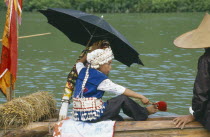 Young boy in costume sitting under umbrella on dragon boat during festival