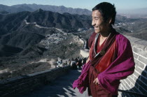 Tibetan Monk standing at the top of steps on The Great Wall which spans the hilly landscape beyond