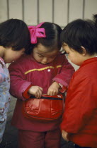 Three young Chinese children looking in handbag wearing red and pink.