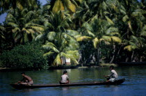 Backwaters. Three people in a canoe passing palm lined banks