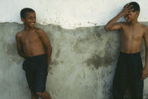 Two wet boys wearing jeans leaning against wall and laughing to each other