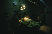 Woman in labour lying on an operating table at the maternity hospital with lamps above her belly