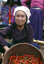 Dai market woman sitting by basket of red chillies